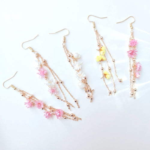 Boucles d’oreilles Élise en fleurs séchées, ornées de chaînes dorées et de perles délicates, disponibles en blanc, rose, et jaune.