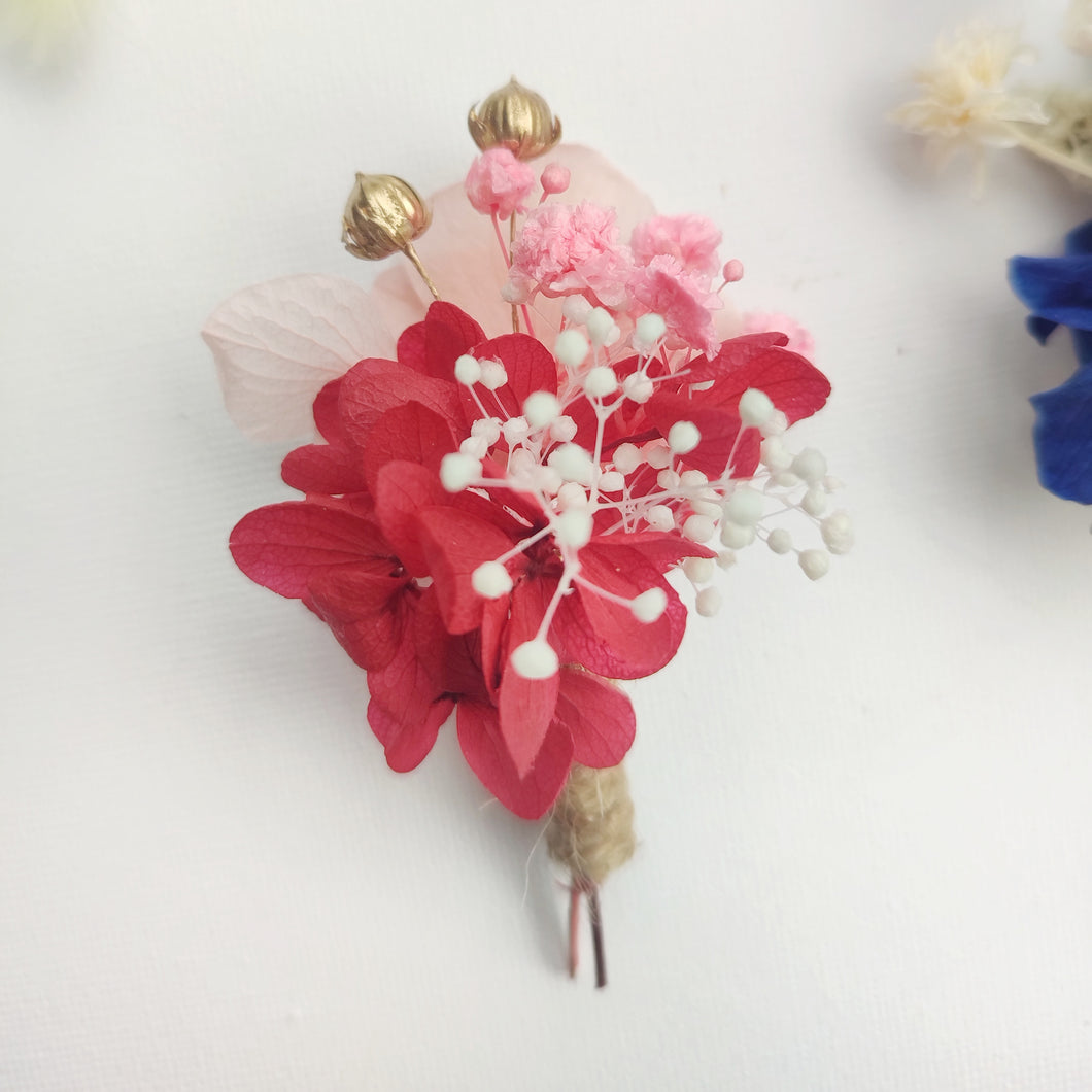 Boutonnière florale rouge avec fleurs éternelles et gypsophile blanc.