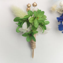 Charger l&#39;image dans la galerie, Boutonnière florale verte avec des petites fleurs blanches et une plume décorative.
