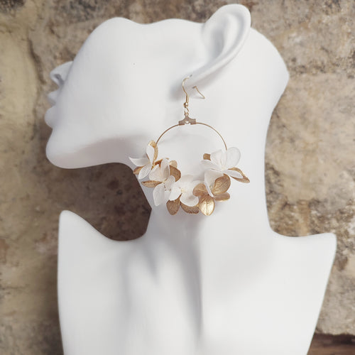 Boucle d'oreille en fleurs stabilisées et séchées Alcina, portée sur un modèle, avec une combinaison de pétales blancs et dorés.